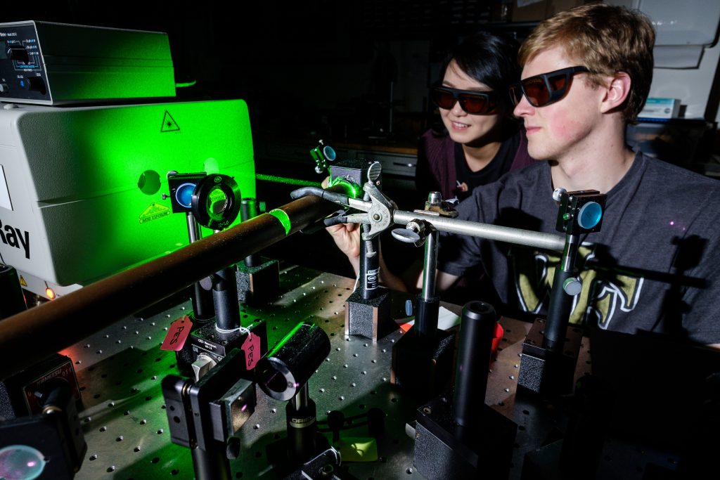 Wake Forest physics graduate students Peiyun Li and Drew Onken work with a sapphire laser to study crystals that can detect gamma rays, in a lab in Olin